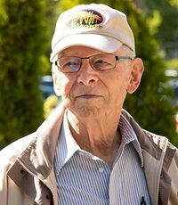 Author J.B. Rivard photo: older white man, wearing a khaki baseball cap, eyeglasses, khaki jacket, and blue button-down shirt