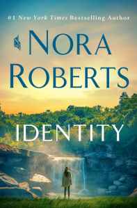 IDENTITY by Nora Roberts book cover featuring an illustrated depiction of mountains, a waterfall and lake/river front with a woman standing on the shoreline