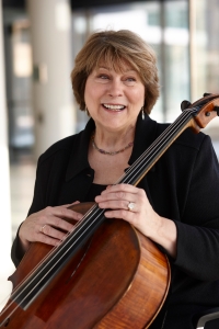 Marcia Peck author photo: smiling seated white female wearing a black top, holding a cello